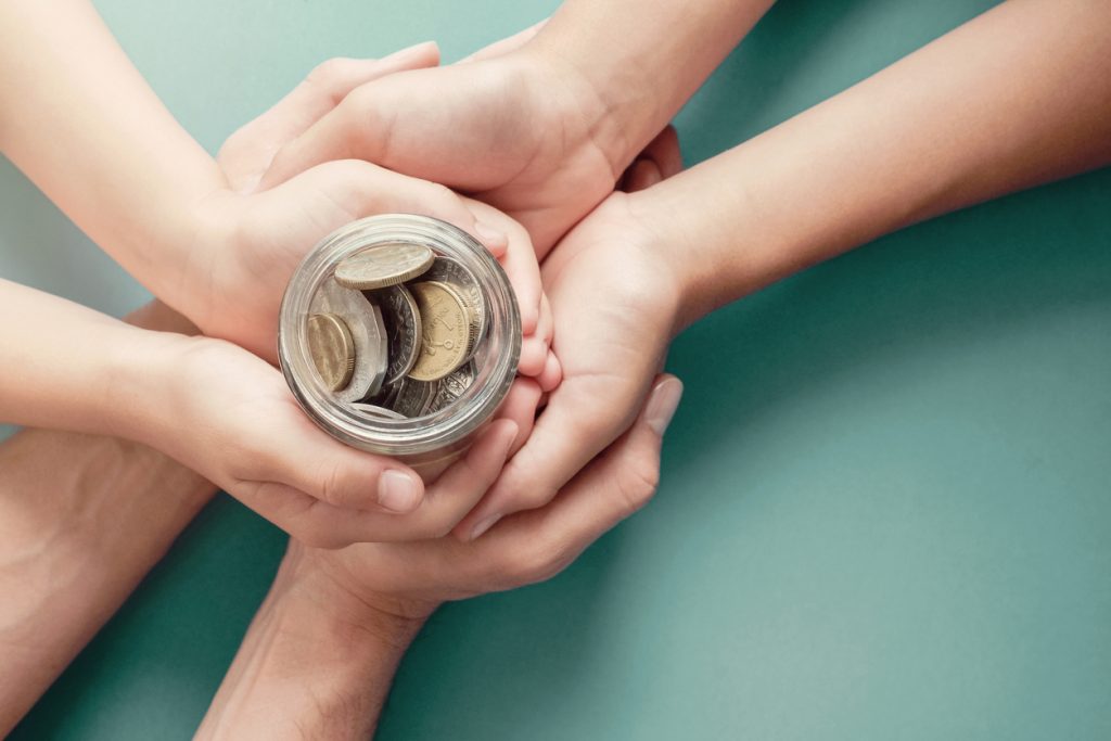 child & parent hands holding money jar